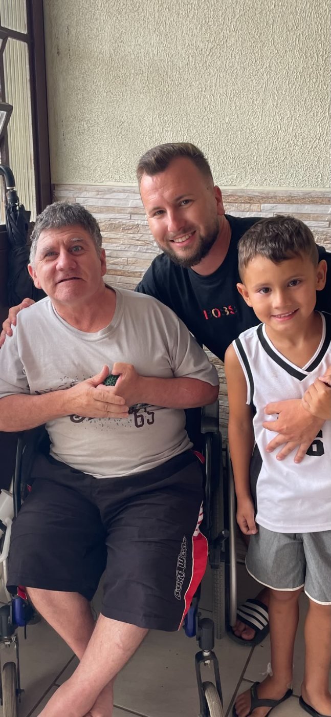 Renan e o filho ao lado de um morador em cadeira de rodas na varanda do Lar